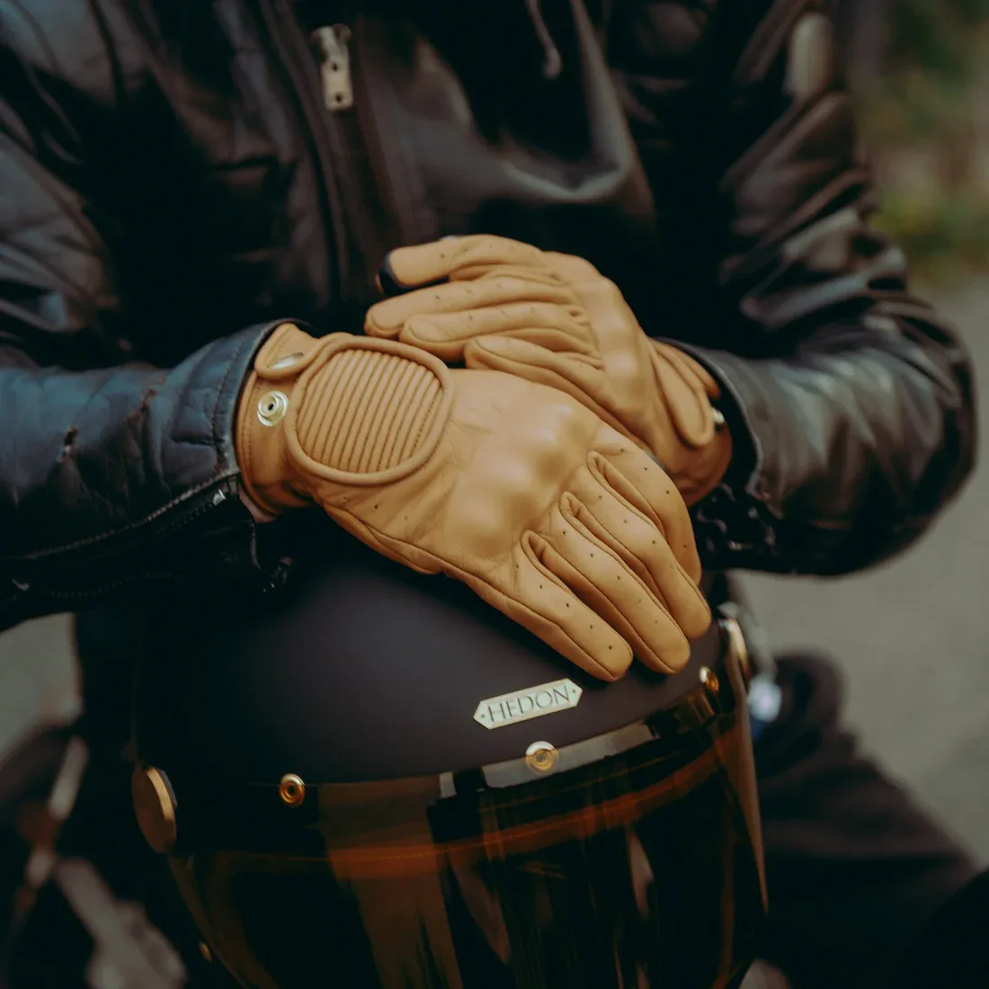Rider wearing tan leather motorcycle gloves over a black Hedon helmet